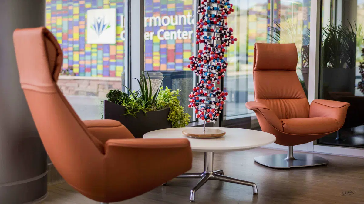 a dna helix on a table between two orange chairs, in a plantscaped room