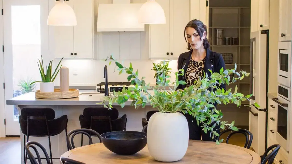 a woman sitting at a counter behind a uniquely shaped pot growing a plant