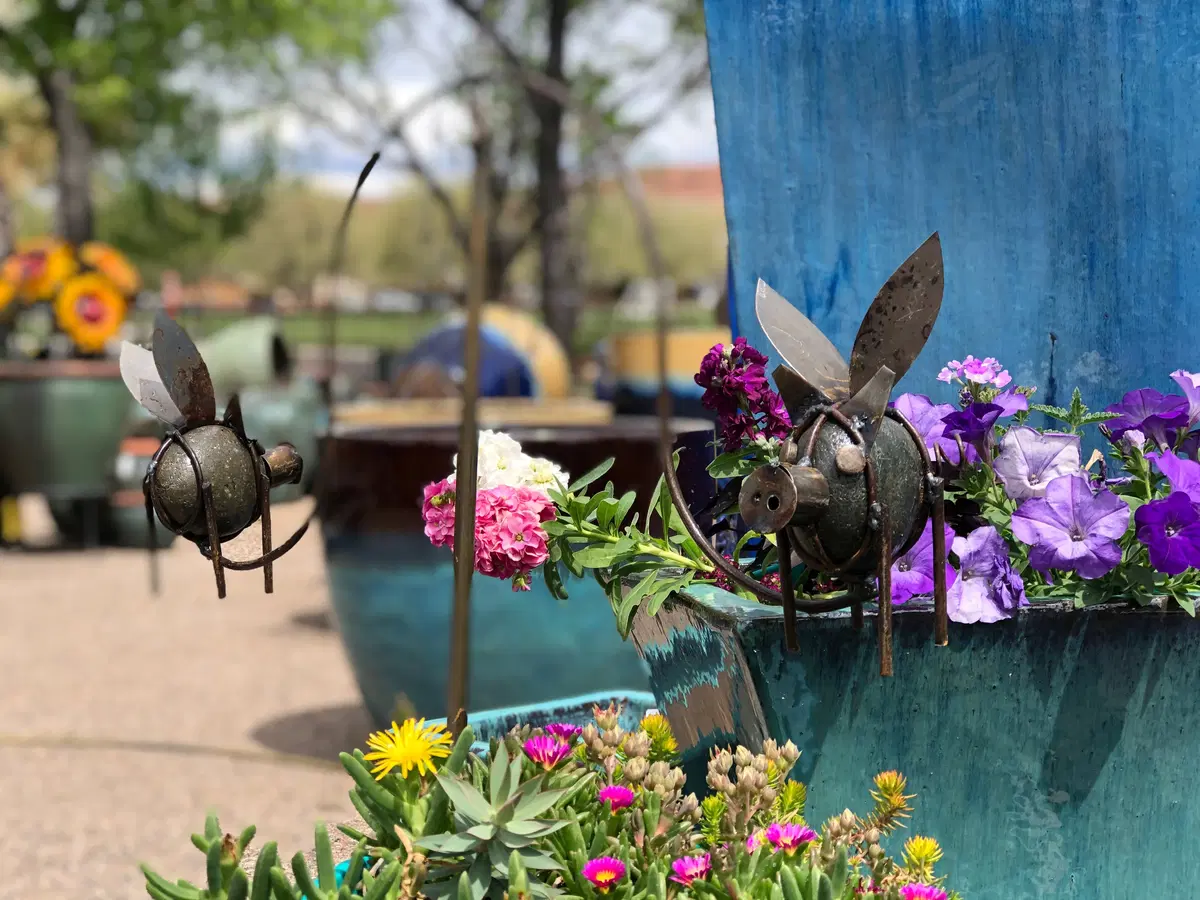 metal flying insects hanging above a pot planted with colorful flowers