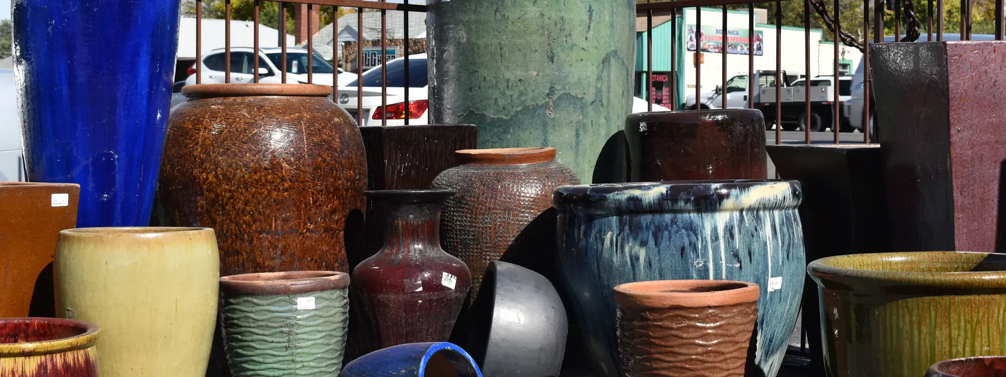 a display of outdoor ceramic pottery in front of a rustic metal fence