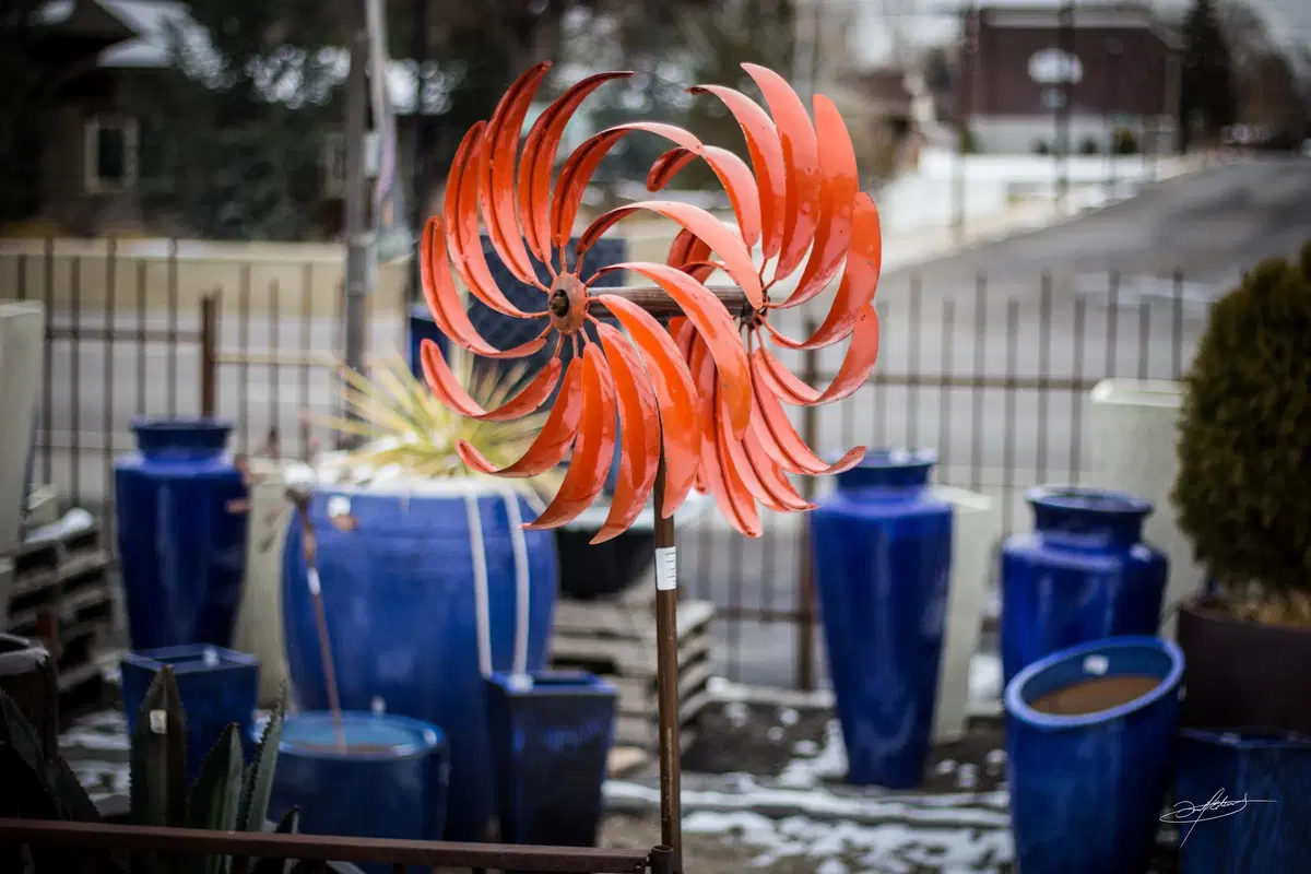 an orange metal windmill spinning in the wind, with blue pottery in the foreground